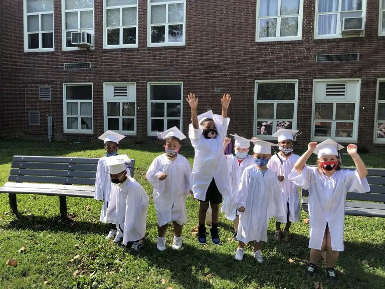 A group of children in graduation attire standing on the grass.